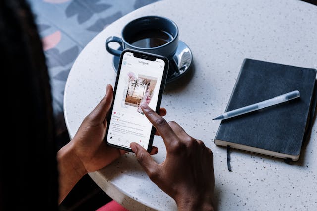 شخص يتصفح موجز Instagram مع كوب قهوة من السيراميك الأسود في مكان قريب.