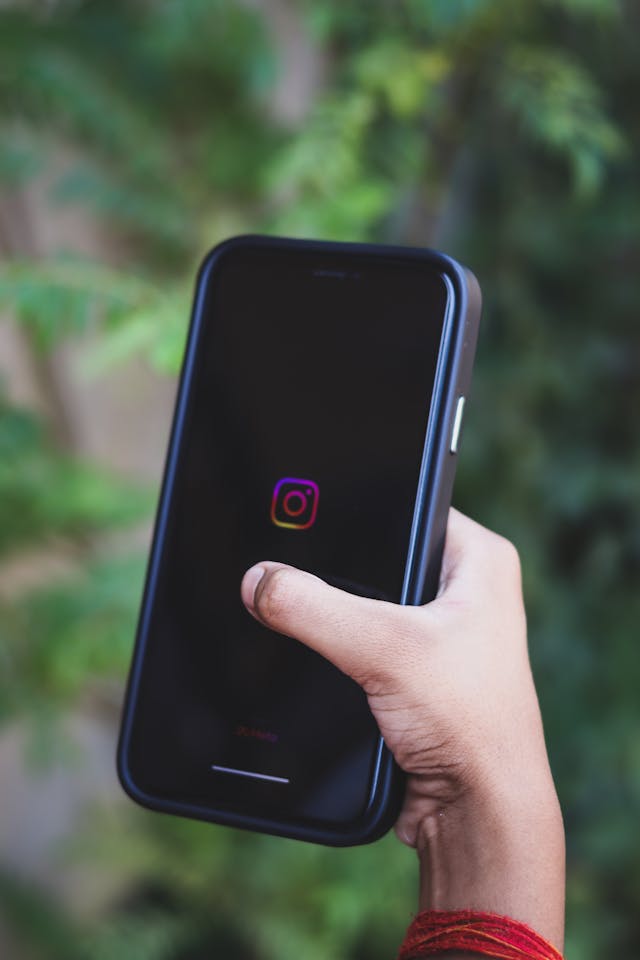 شخص يحمل هاتفًا ذكيًا بشاشة سوداء يظهر عليها شعار Instagram.
