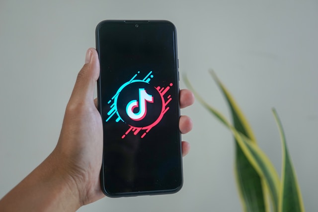 شخص يحمل هاتفًا ذكيًا يتوسطه شعار TikTok في منتصف دوائر نصف حمراء وزرقاء.
