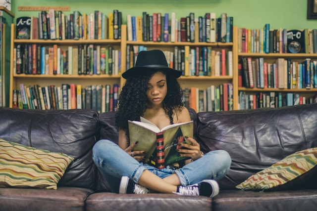 امرأة تجلس القرفصاء على أريكة وتقرأ كتاباً.