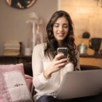 شخص يجلس على أريكة ويبتسم بينما ينظر إلى هاتفه.