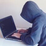 مخترق يرتدي سترة بقلنسوة ويكتب كوداً على حاسوبه المحمول.