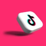 نرد أبيض على خلفية مائلة للوردي مع شعار TikTok عليه.