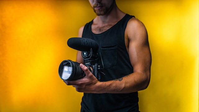 رجل يرتدي قميصاً أسود بدون أكمام ويحمل كاميرا DSLR.