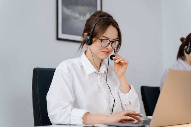 Frau im weißen Hemd spricht in das Mikrofon ihres Headsets.
