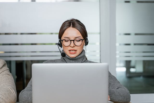 Frau im grauen Pullover spricht in ihr Mikrofon und trägt ein Headset.