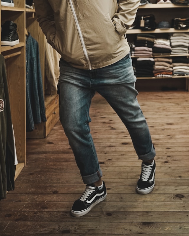 Eine Person, die eine blaue Jeans, eine beige Jacke und schwarz-weiße Turnschuhe trägt.