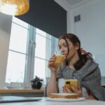 Eine Frau benutzt ein Smartphone, während sie ein Glas Saft trinkt.