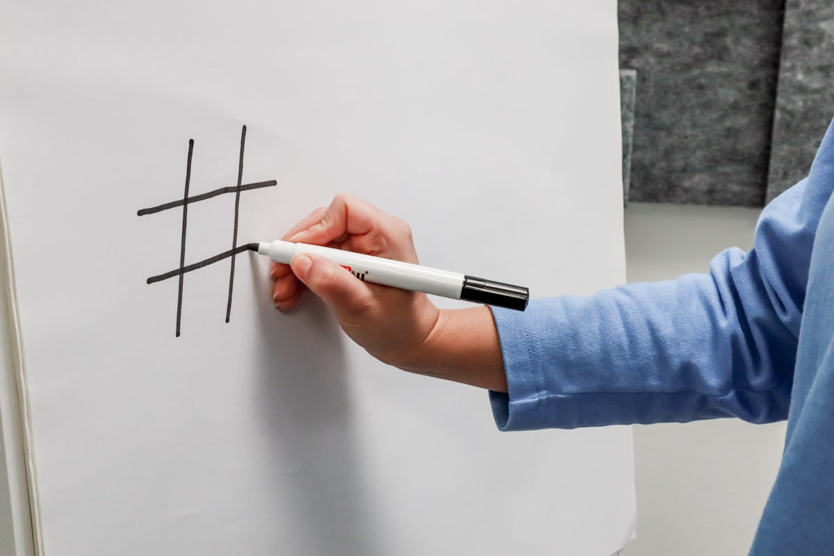 Eine Person zeichnet ein schwarzes Hashtag auf ein weißes Blatt Papier.