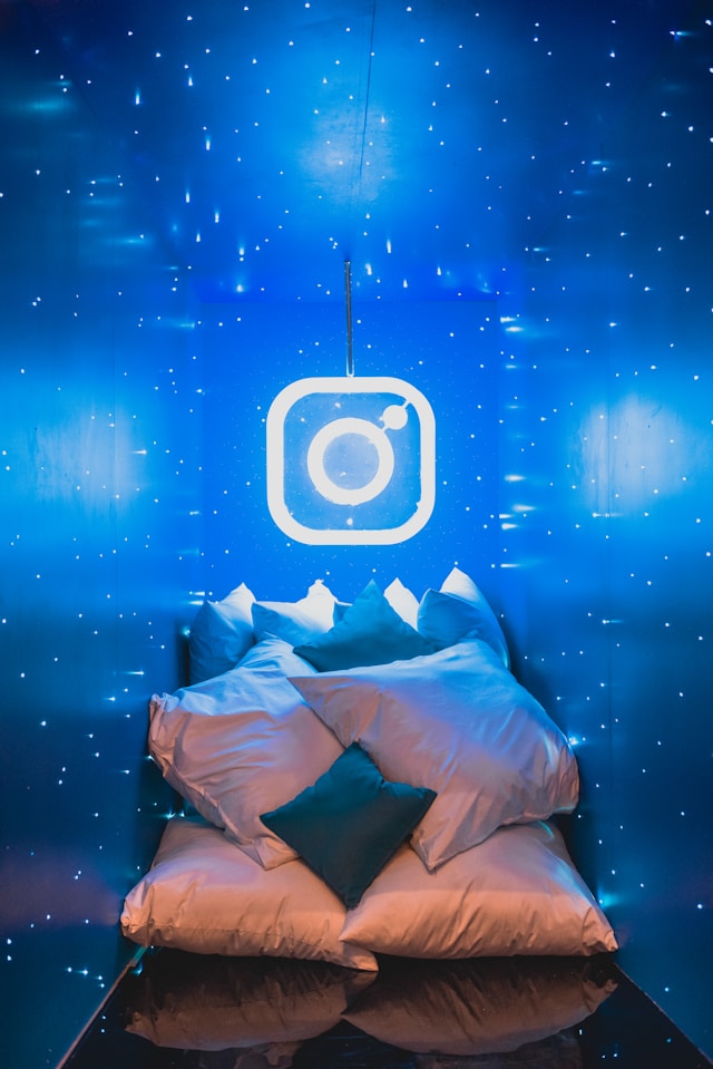 Ein weißes Neonschild mit dem Instagram-Logo an einer blauen Wand mit vielen Kissen darunter.