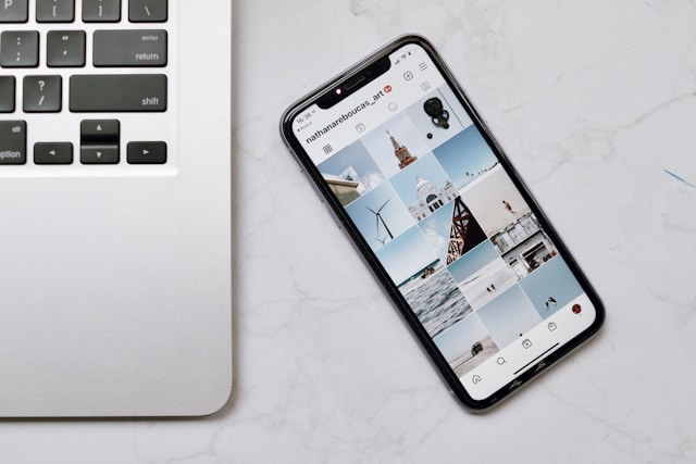 Ein Smartphone, das einen Instagram-Feed anzeigt, steht neben einem Laptop auf einem Tisch.