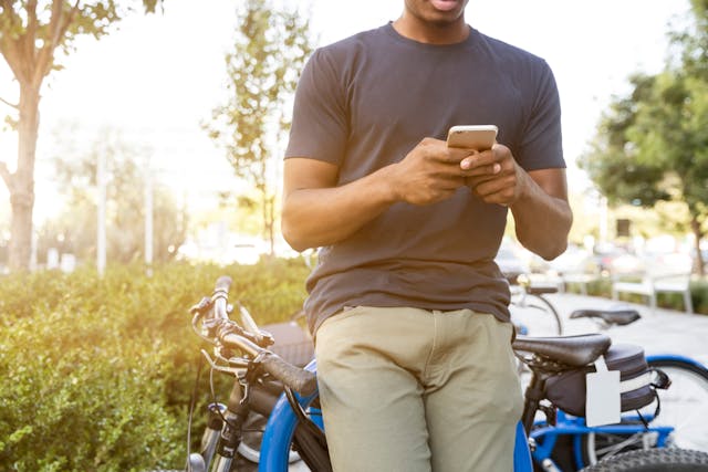 Ein Mann, der auf seinem Fahrrad sitzend durch sein Handy scrollt.