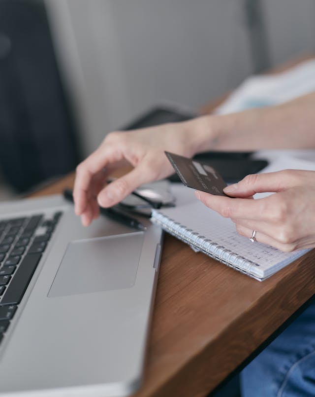Eine Person, die ihren Laptop benutzt und eine Bankkarte in der Hand hält.