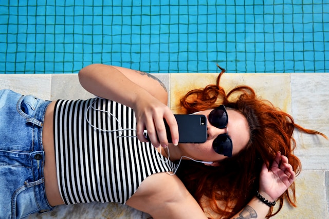 Eine Person, die Musik hört, während sie telefoniert und sich an einen Pool legt.