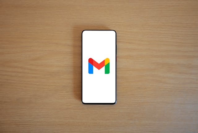 Ein Smartphone auf einem Holztisch mit dem Gmail-Logo auf dem Bildschirm.