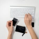 Eine Person, die eine Kreditkarte in der einen Hand hält und mit der anderen auf einer Computertastatur tippt, um etwas online zu kaufen.