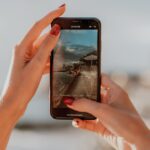 Un smartphone muestra una imagen nítida de una playa y el dedo de una persona se cierne sobre el botón de grabación.