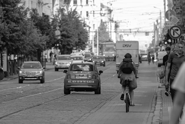 Plano en blanco y negro desde una ciudad ajetreada con coches en movimiento en la carretera y peatones en la acera.