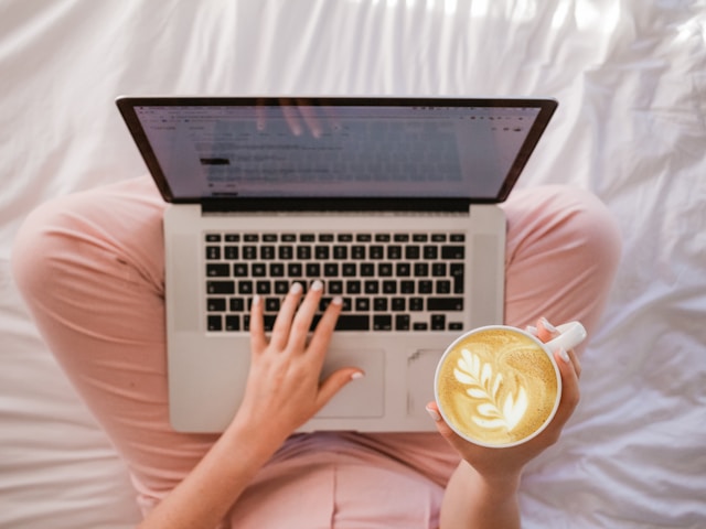 Imagen superior de una persona que utiliza un Macbook Pro y sostiene una taza de capuchino.