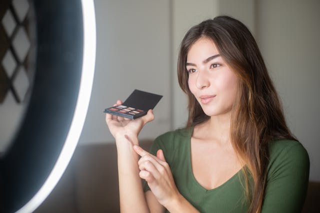 Una persona grabándose y mostrando productos de maquillaje.