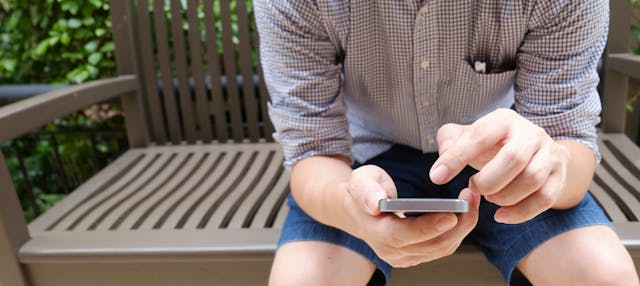 Un homme assis sur un banc et faisant défiler son téléphone.