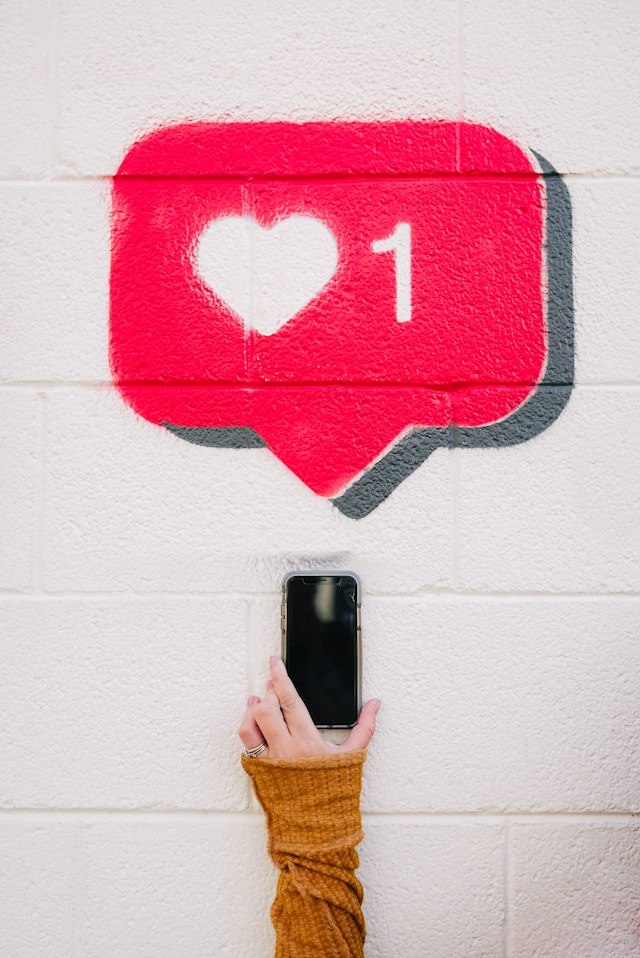 Graffiti mural d'un "like" Instagram et d'une main posant avec un téléphone en dessous.