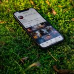 Un smartphone posé sur un sol herbeux avec un flux Instagram affiché sur l'écran.