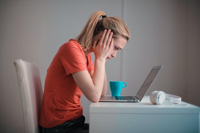 Une personne assise devant un ordinateur portable avec une tasse de café, l'air soucieux.