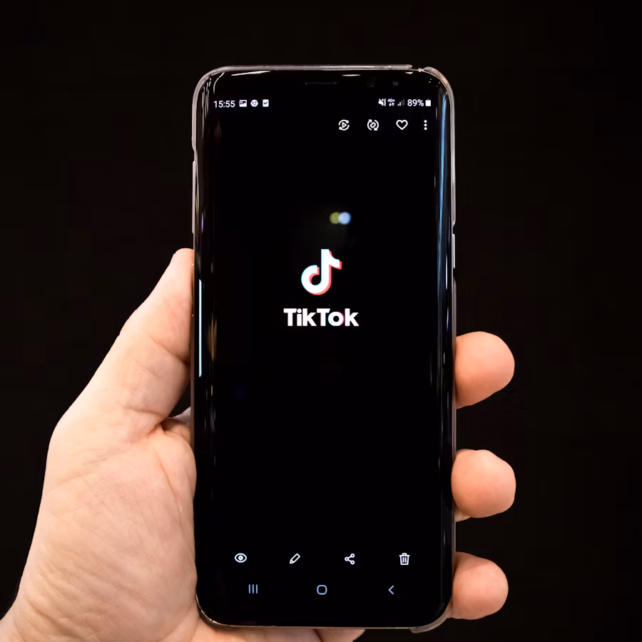  Une personne tenant un smartphone sur lequel apparaît le logo TikTok sur un écran noir. 