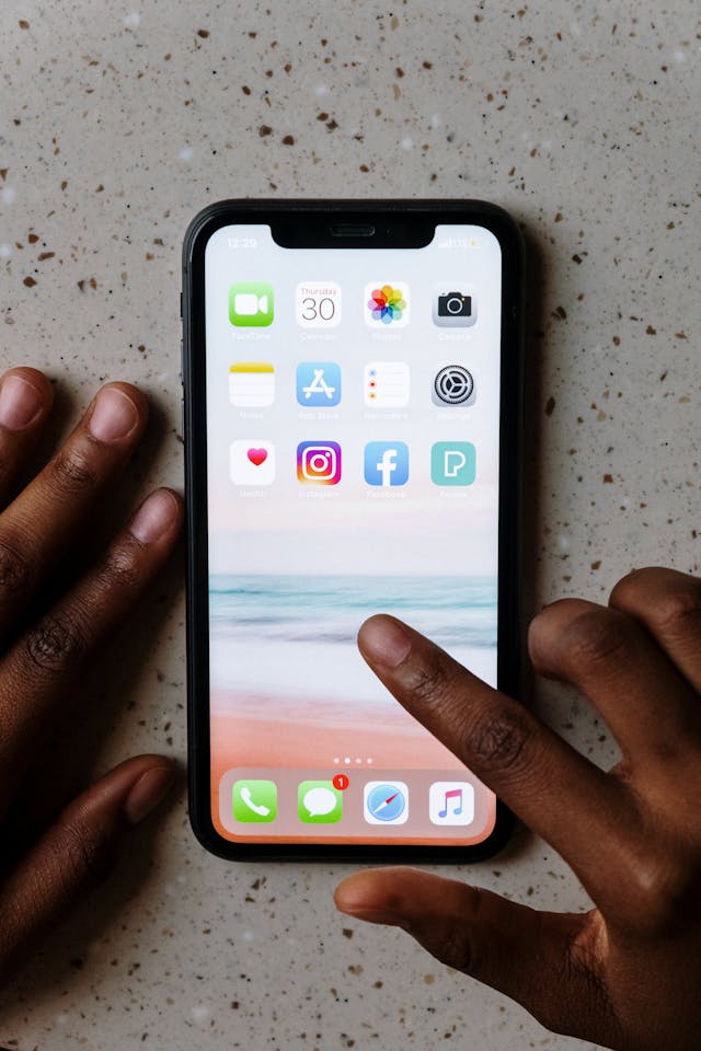 Un smartphone posé sur une table et une personne qui s'apprête à cliquer sur une application.