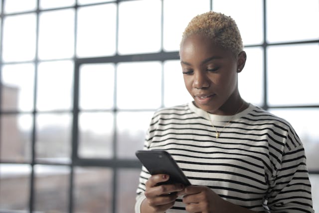 Une femme avec un haut rayé regardant son smartphone.
