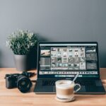 Un ordinateur portable équipé d'un logiciel de montage, avec une tasse de café devant lui et un appareil photo à côté.