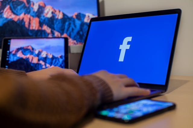 Une personne utilisant un ordinateur portable avec le logo de Facebook affiché sur l'écran.
