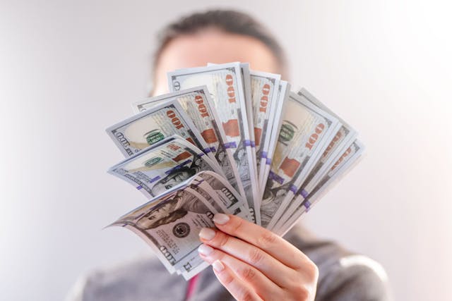 Une personne tenant un éventail de billets de banque et se couvrant le visage avec.