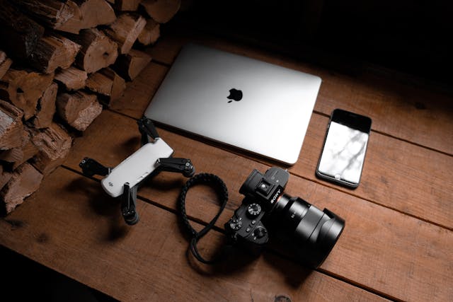 Un treppiede, un telefono, una fotocamera e un computer portatile posizionati su un tavolo.
