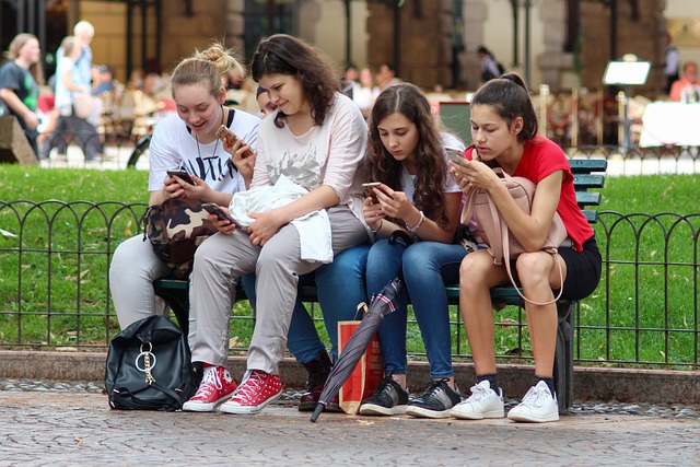 Un gruppo di quattro adolescenti seduti su una panchina che usano il cellulare.