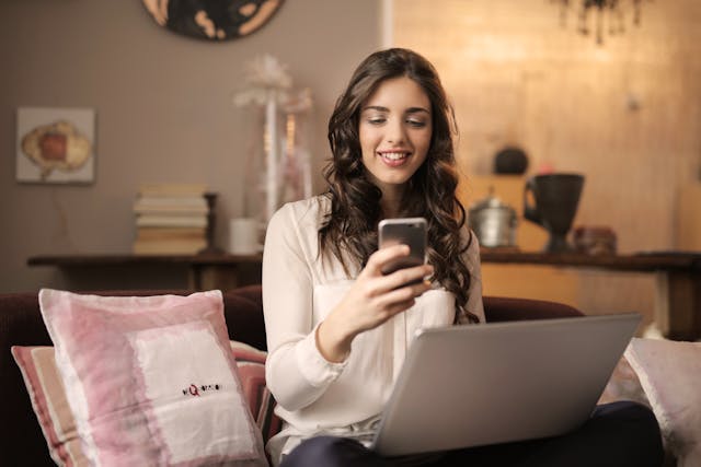 Una persona che guarda il proprio telefono, con un computer portatile sulle ginocchia.