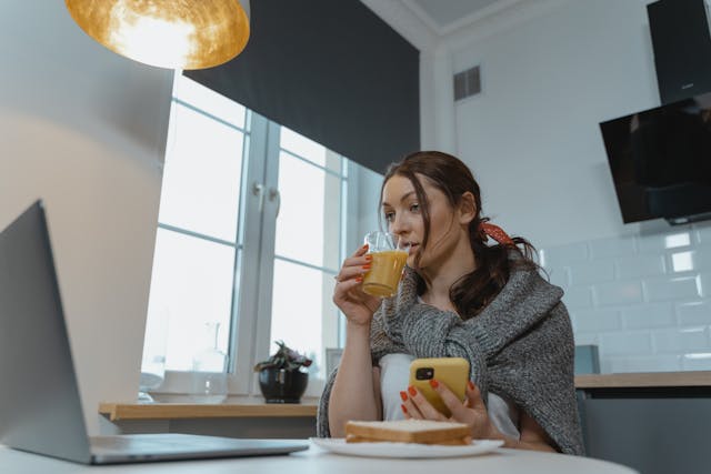 Una donna che usa lo smartphone mentre beve un bicchiere di succo di frutta.