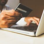 Una persona al portatile con in mano una carta di credito.