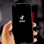 Una persona che tiene in mano uno smartphone con la cornice di apertura di TikTok visualizzata sullo schermo.