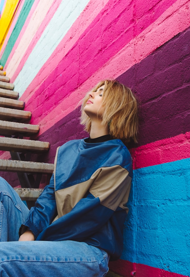 Una donna seduta appoggiata a un muro colorato.