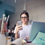 Una persona seduta accanto a un computer portatile mentre guarda il proprio telefono.