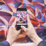 Una persona che utilizza uno smartphone per scattare una foto di un muro graffitato.