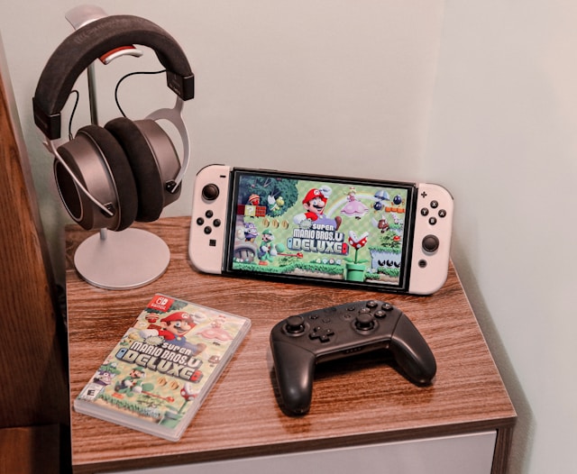 Un sistema di gioco, un controller e delle cuffie su un mobile di legno.