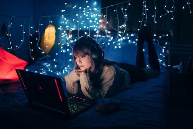 Una persona sdraiata sul letto la sera mentre guarda il suo computer portatile.