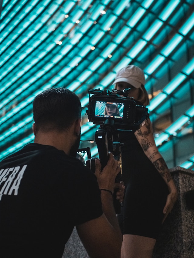Un uomo in camicia nera con in mano una fotocamera DSLR.