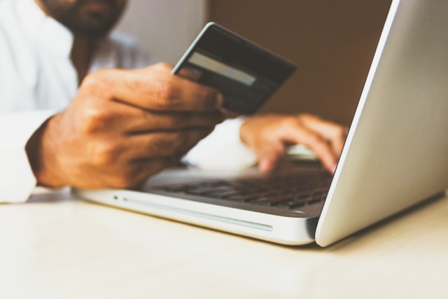 Una persona che guarda la propria carta di credito mentre utilizza un computer portatile.