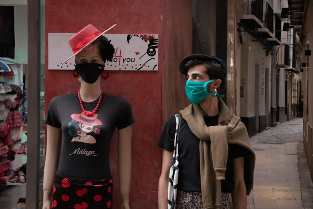 Um homem com uma t-shirt preta e uma máscara verde, de pé ao lado de um manequim.