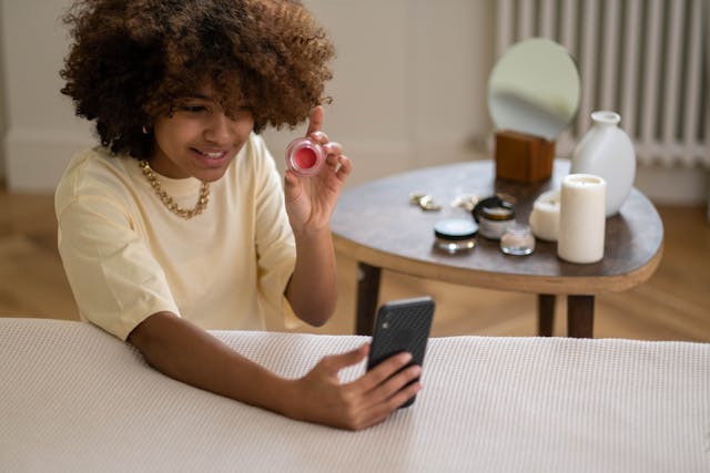 Uma pessoa mostra produtos de beleza enquanto se grava a si própria no seu telemóvel.