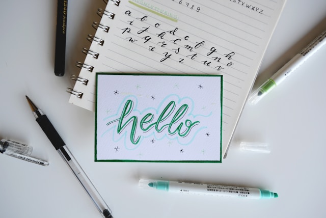 A palavra "Hello" desenhada em papel branco com um marcador verde e pequenas estrelas pretas à volta.